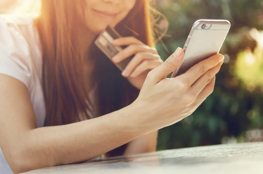 携帯電話を見つめながら、クレジットカードを手にした少女