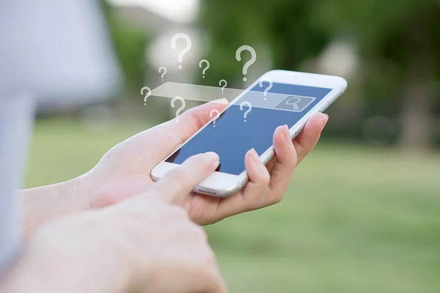 検索バーが空で、たくさんの疑問符が表示されたスマートフォンを手に持っている手