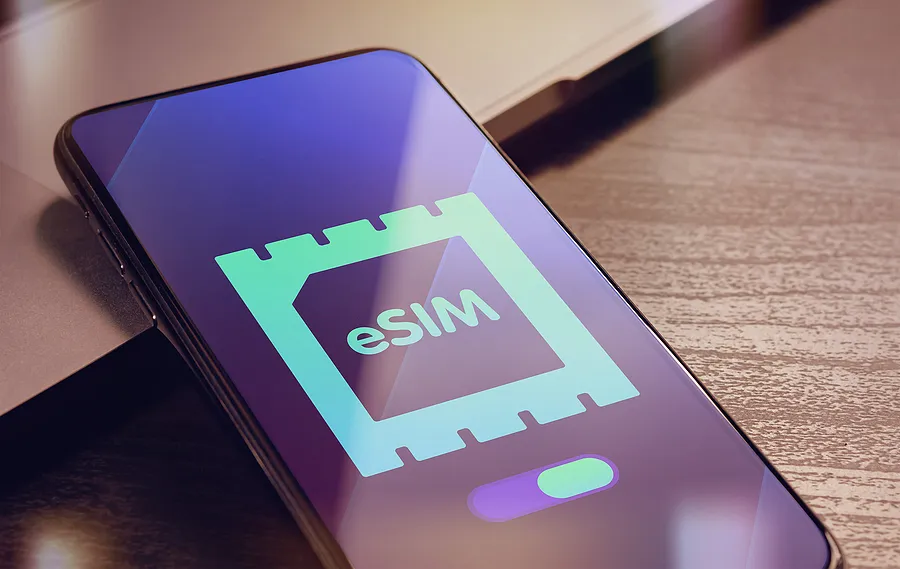 机の上に置かれたスマートフォンに、eSIMカードのロゴが表示されている