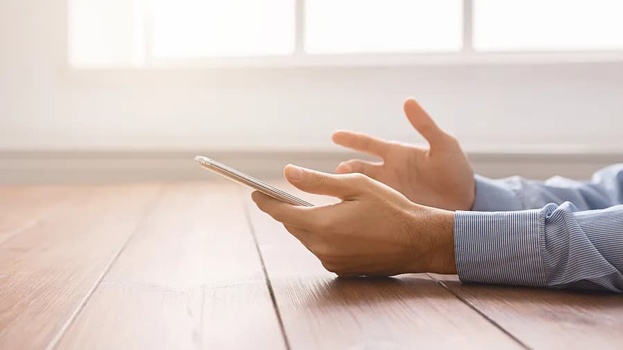 窓辺でiPhoneを手にしている人物。これは、パソコンを使わずにiPhoneのパスコードを解除する方法を示しています。