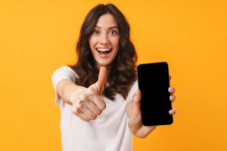 スマートフォンを手に持ち、親指を立てて笑顔を見せる女性。これは、電話による本人確認と認証手続きが成功したことを象徴している。