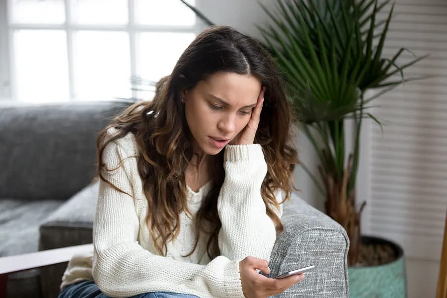 スマートフォンを眺める心配そうな女性の姿。これは、中古スマホを購入する前に、その端末のレポートを確認し、利用履歴を把握することの重要性を表しています。